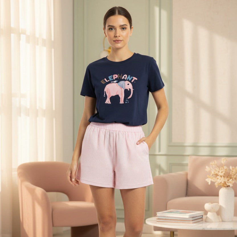 Woman wearing a navy tshirt with an elephant graphic and pink shorts in a modern living room