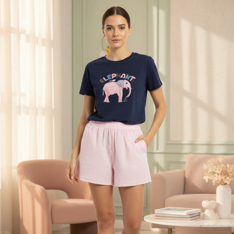 Woman wearing a navy tshirt with an elephant graphic and pink shorts in a modern living room