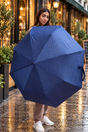 Woman holding open a navy herringbone folding umbrella on a wet street