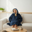 Person wearing a navy hooded blanket sitting on a couch in a cozy living room.