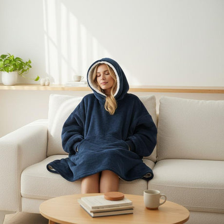 Person wearing a navy hooded blanket sitting on a couch in a cozy living room.