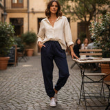 Woman in a white shirt and navy pants walking in an outdoor setting with tables and chairs