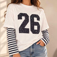 Woman in a white tee with a distressed navy 26 print and navy striped long sleeves