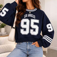 Woman in a cropped navy Los Angeles 95 varsity sweatshirt with white striped sleeves