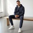Man sitting on a wooden bench wearing a navy tracksuit and white sneakers