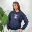 Woman wearing a navy crew neck sweatshirt with white Mountain Station lettering and light jeans