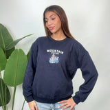 Woman wearing a navy crew neck sweatshirt with white Mountain Station lettering and light jeans