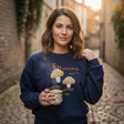Woman wearing a navy sweatshirt with golden embroidered mushrooms and amber lettering