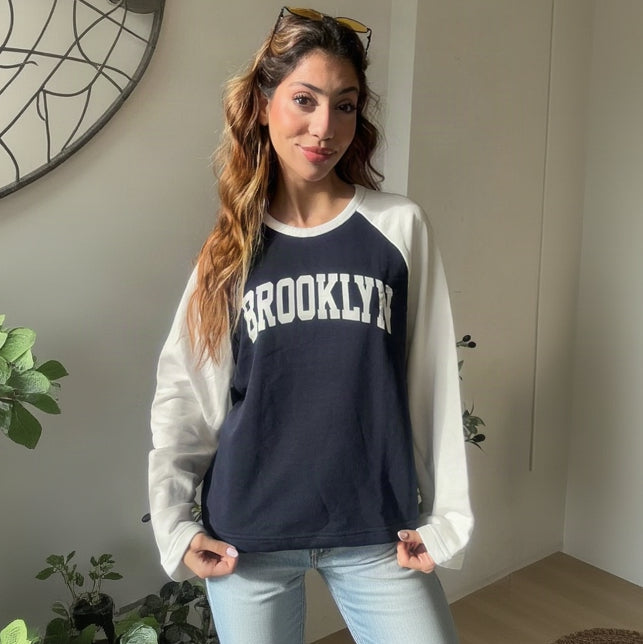 Woman wearing a navy and white raglan Brooklyn sweatshirt with light wash jeans