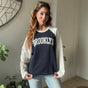 Woman wearing a navy and white raglan Brooklyn sweatshirt with light wash jeans