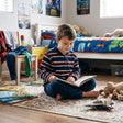 Boy sitting on a rug in a navy, red and white striped fleece pyjama set with navy bottoms