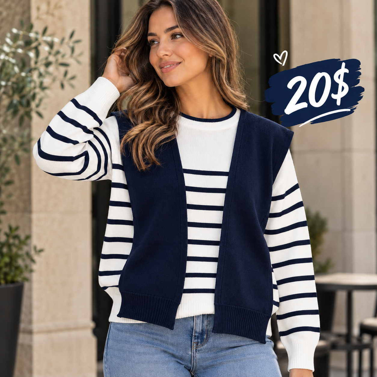 Woman in a white and navy striped sweater with an attached navy vest layer and blue jeans outside a stone building