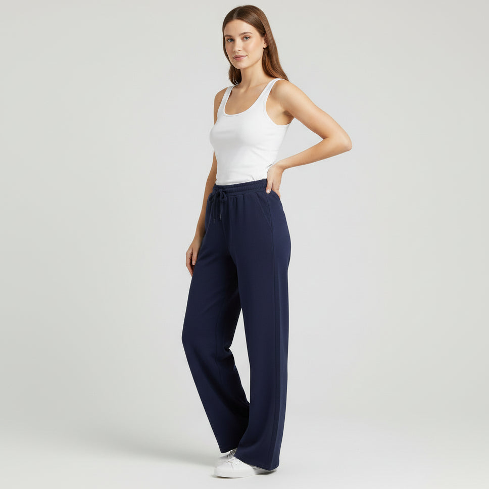 Woman wearing navy wide-leg pants and a white tank top on a light gray background