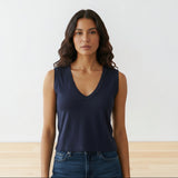 Woman wearing a navy blue tank top and jeans against a white wall