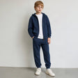 Boy in glasses wearing a navy zip hoodie and joggers over a white tee