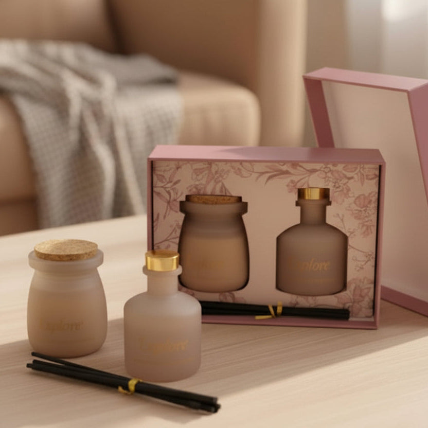 Pale greige frosted diffuser and candle beside a dusty rose box of black reeds