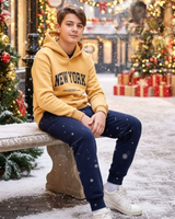 Teen boy in a mustard New York hoodie and navy joggers on a snowy bench