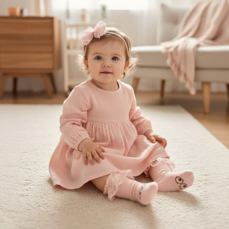 Infant in a blush dress wearing a pale pink tulle bow headband with matching face print knee socks