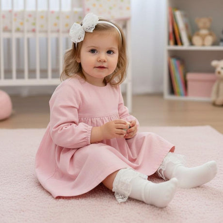 Baby girl in a pink dress wearing a white lace bow headband and white ribbed socks with lace frill cuffs