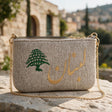 Close view of a plush oatmeal bag with a large green cedar and gold Arabic lettering, on a rough stone surface
