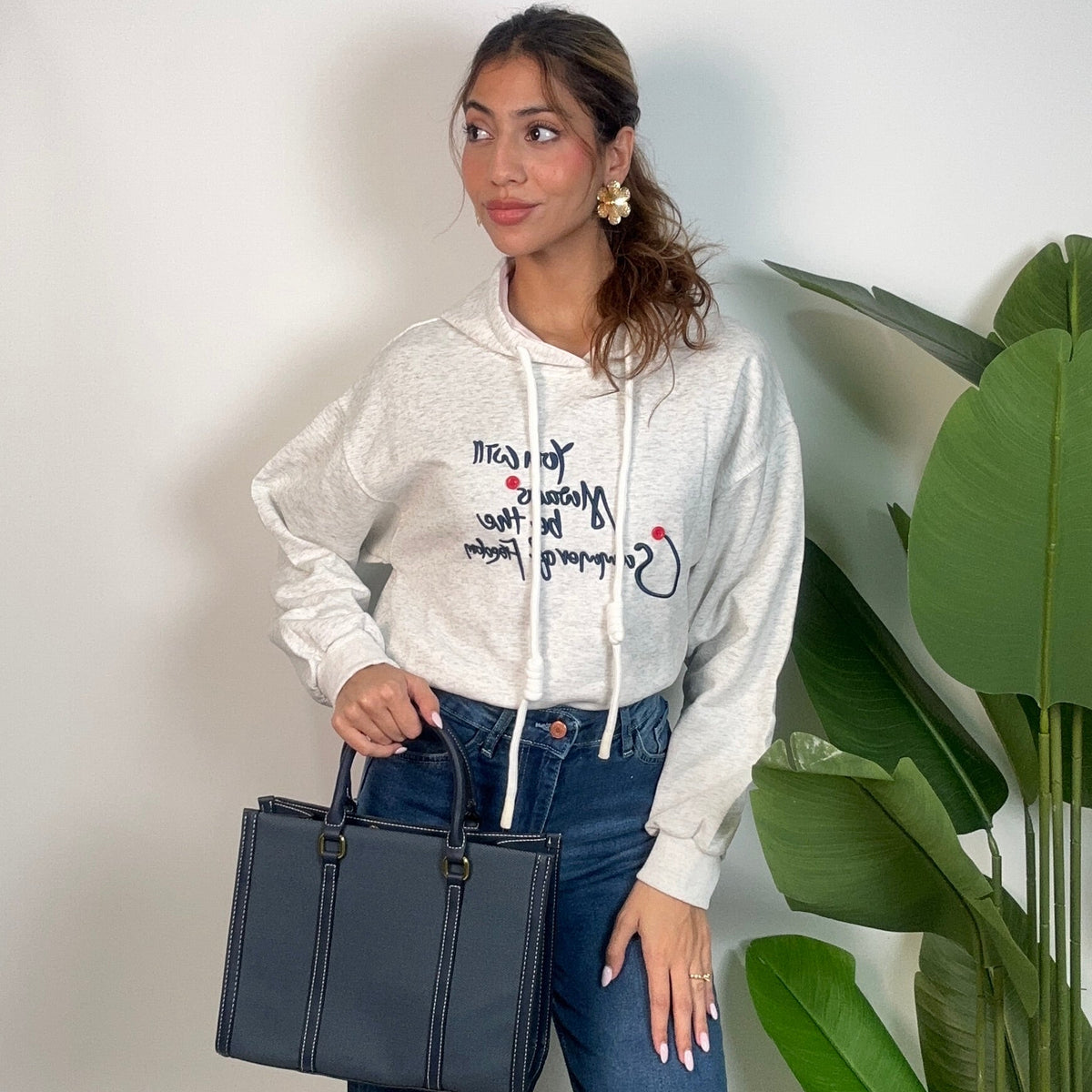 Oatmeal cropped hoodie styled with a navy structured handbag and jeans