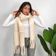 Woman wearing an off white brushed blanket scarf looped around her neck with long tassel ends