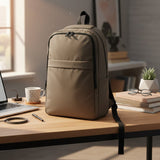 An olive backpack with black zippers and straps sits on a wooden desk in a bright, modern home office setting