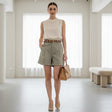 Woman in a beige sleeveless top and olive green shorts standing in a minimalistic room
