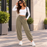 Woman in olive green cuffed joggers with a drawstring waist, a long sleeve white crop top and white sneakers