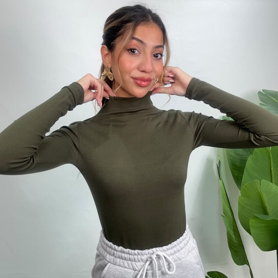 Olive turtleneck tucked into grey drawstring joggers, hands at the neckline