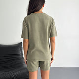 Person wearing an olive green tshirt and shorts set against a neutral background