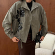 Olive green oversized jacket with black sequin flowers, an open snap collar and belted hem