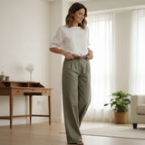 Woman wearing a white top and olive green pants in a bright living room