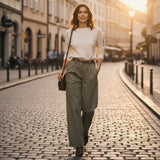 Woman wearing olive wide-leg pants and white sweater walking on a cobblestone street in an urban setting
