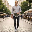 Man walking on a street with a green bag, surrounded by trees and buildings.