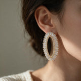 Woman with hair tied back wearing a gold tone open oval crystal statement earring