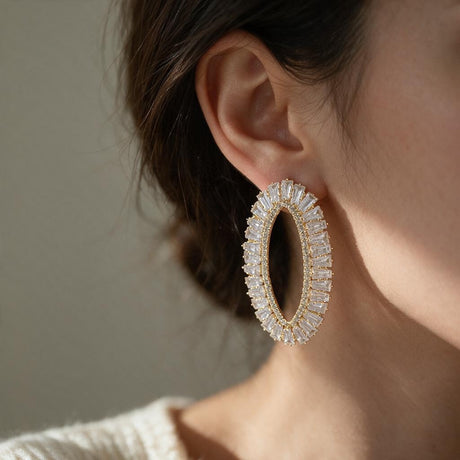 Woman with hair tied back wearing a gold tone open oval crystal statement earring