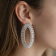 Silver open oval earring lined with clear baguette crystals worn on the ear