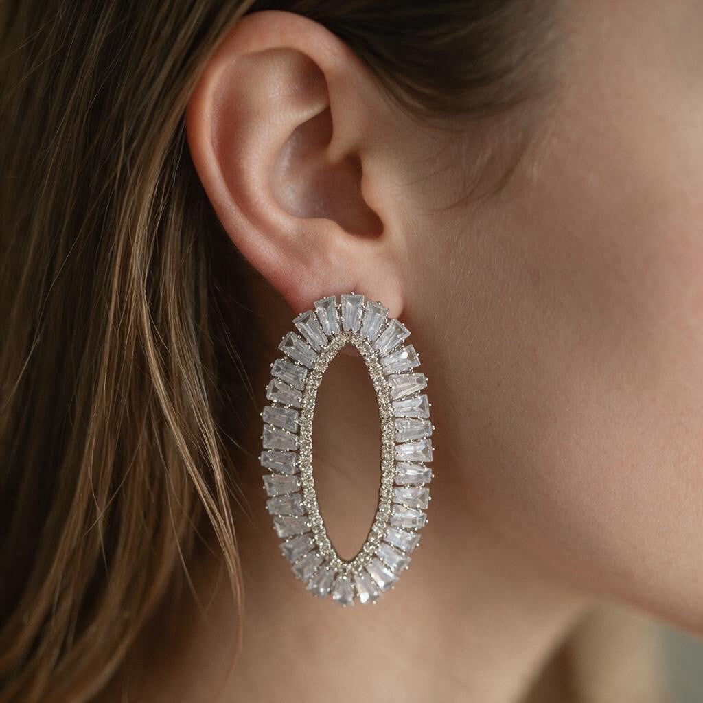 Silver open oval earring lined with clear baguette crystals worn on the ear