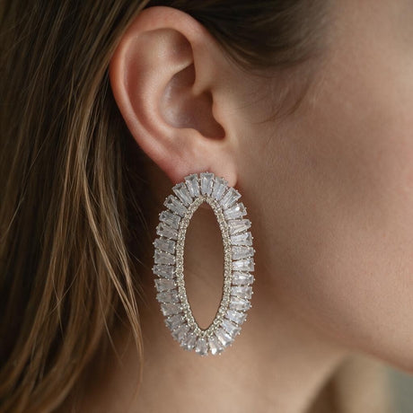 Silver open oval earring lined with clear baguette crystals worn on the ear