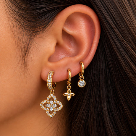 Ear wearing a pave hoop with a large open crystal quatrefoil drop, a small gold flower and a round crystal