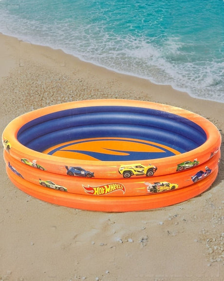 Orange three ring inflatable kids pool with race car graphics and a blue base, set up on a beach