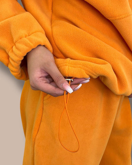 Close-up of a person wearing an orange fleece outfit with a beige background