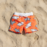 Orange swim shorts with shark pattern on sandy surface