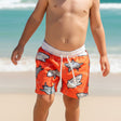 Child wearing orange swim shorts with shark pattern on a beach