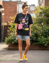 Woman wearing a black tshirt with a mickey mouse graphic design, and denim shorts outdoors