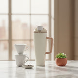 Cream insulated tumbler with a blush handle beside a pour over coffee set