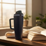 Navy insulated travel tumbler on a wooden table beside an open book