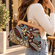 Woman carrying a paisley tapestry handbag with a wooden frame on a gold chain over her shoulder