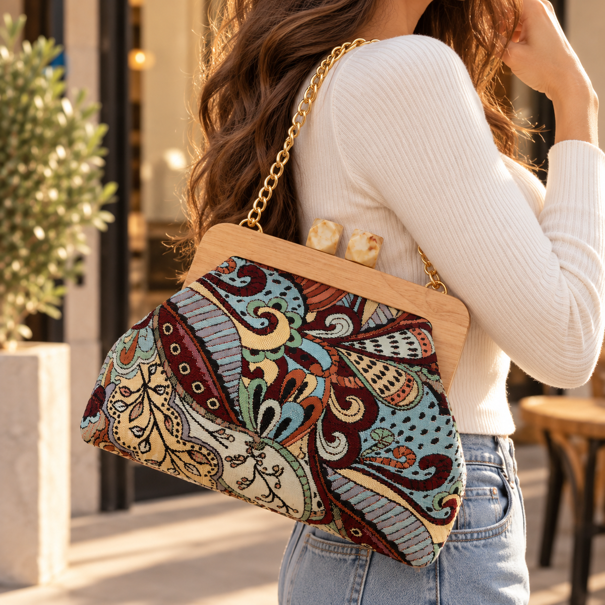 Woman carrying a paisley tapestry handbag with a wooden frame on a gold chain over her shoulder
